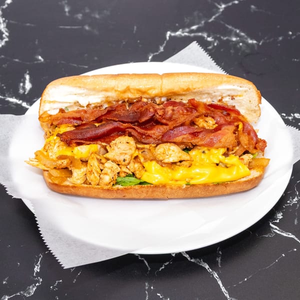 A large chicken and bacon sandwich with melted cheese on a white plate.