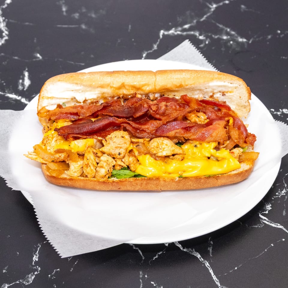 A large chicken and bacon sandwich with melted cheese on a white plate.