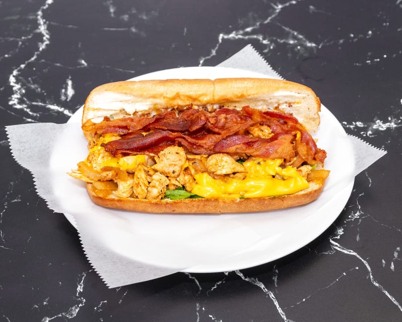 A large chicken and bacon sandwich with melted cheese on a white plate.