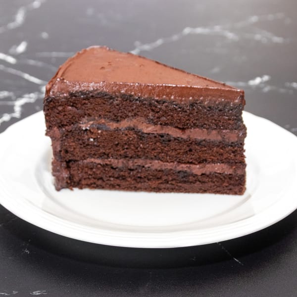 A slice of rich chocolate cake with multiple layers of frosting on a white plate.