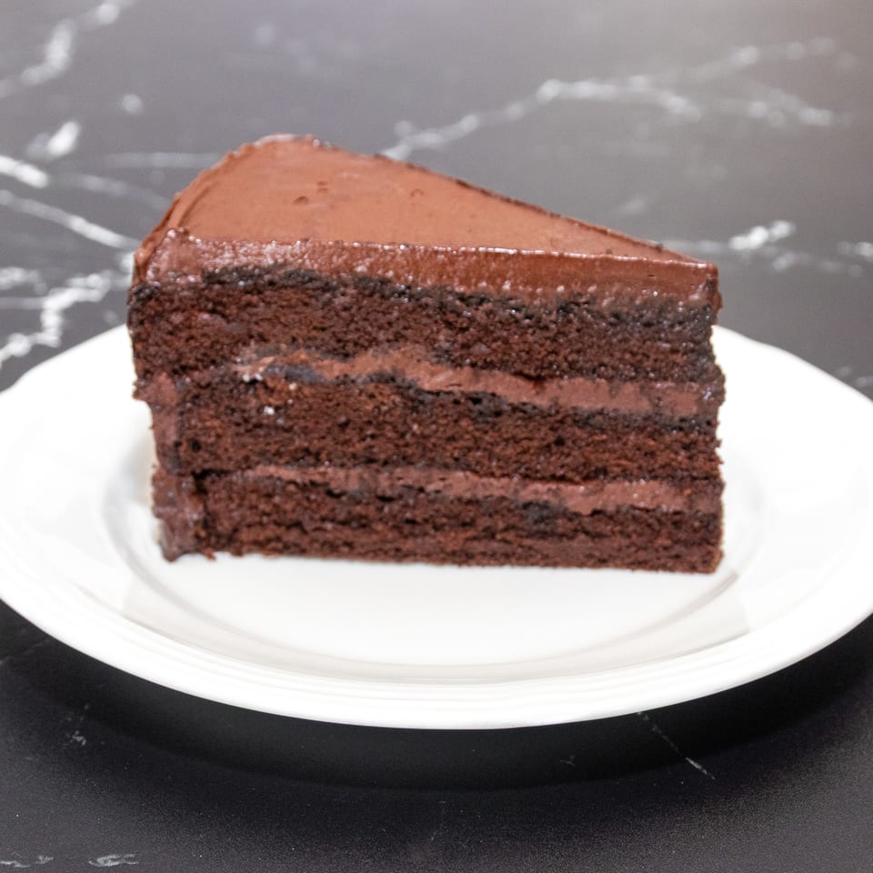 A slice of rich chocolate cake with multiple layers of frosting on a white plate.