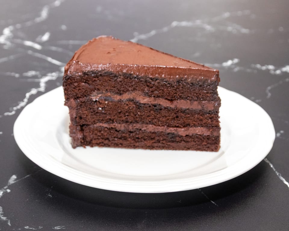 A slice of rich chocolate cake with multiple layers of frosting on a white plate.