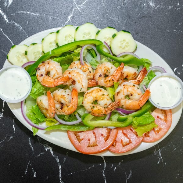 A vibrant shrimp salad with lettuce, tomatoes, cucumbers, onions, and bell peppers, served with two dressing cups.