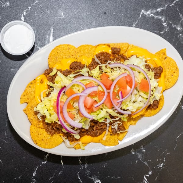 A plate of nachos with ground beef, melted cheese, lettuce, tomatoes, and red onions, with a side of sour cream.