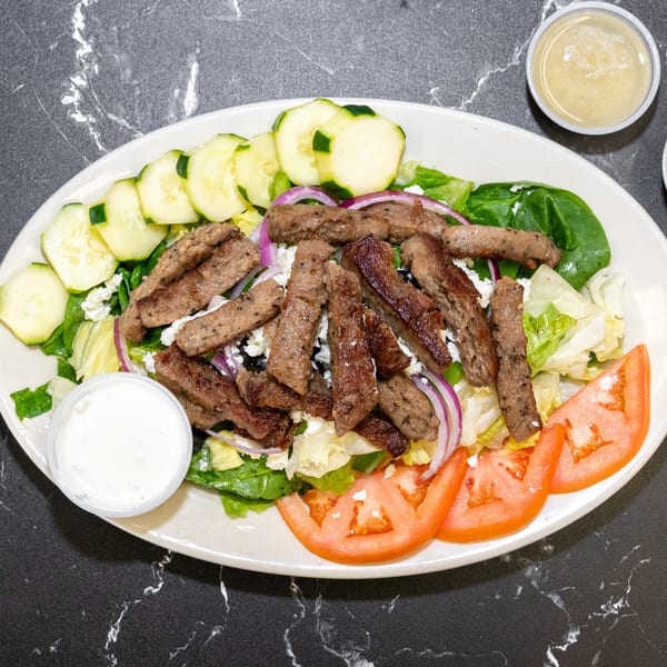 Gyro meat salad with lettuce, cucumbers, tomatoes, red onion, feta, and dressing on a white plate.