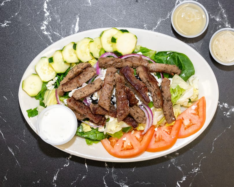 Gyro meat salad with lettuce, cucumbers, tomatoes, red onion, feta, and dressing on a white plate.