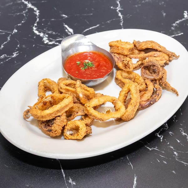 Crispy fried calamari rings and tentacles with a side of red marinara sauce on a white plate.